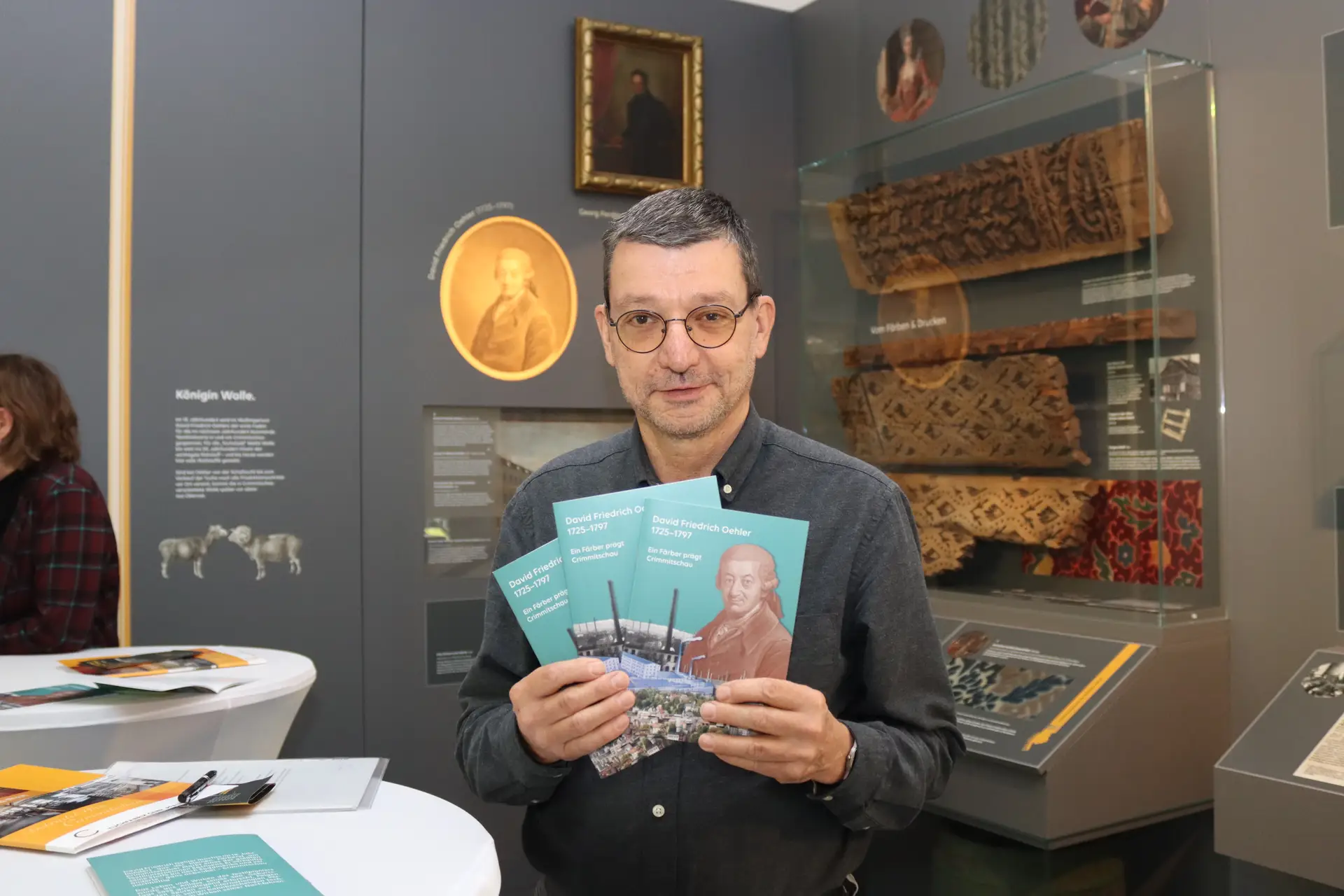 Lutz Hanzig hält mehrere Exemplare der Broschüre vor sich; im Hintergrund sind Ausstellungsvitrinen zu sehen.