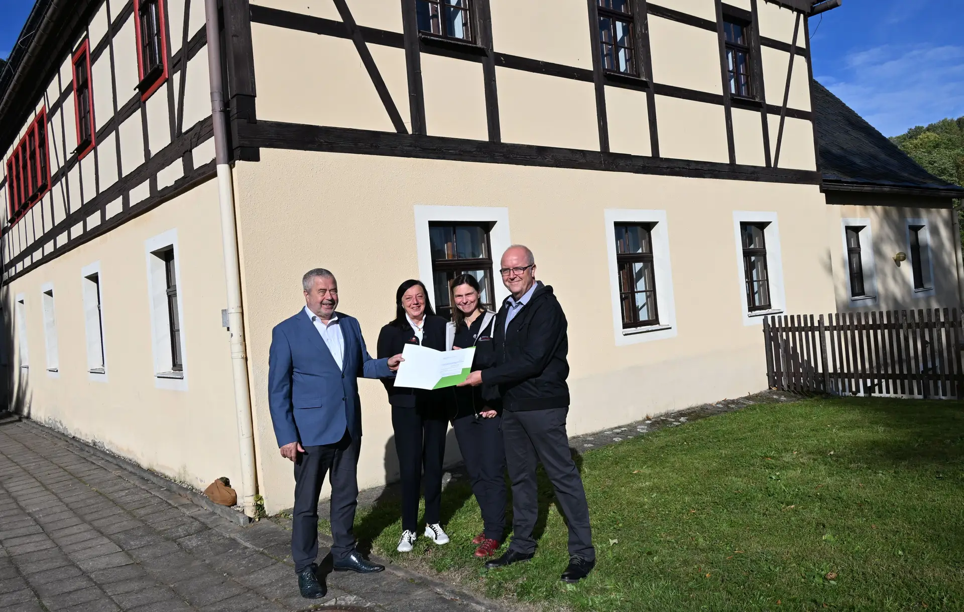 Mehrere Personen posieren nebeneinander. Zu sehen sind ein Landrat, eine stellvertretende Bürgermeisterin und weitere Vertreter beim Übergang eines Zuwendungsbescheids.